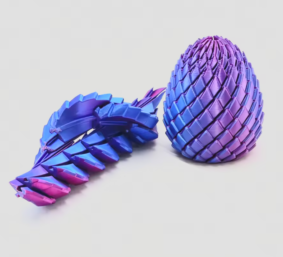 Two 3D-printed articulated toy models, one egg-shaped and one leaf-like, featuring a vibrant blue, purple, and pink iridescent gradient finish, displayed on a clean light gray background.